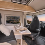Intérieur d'un fourgon aménagé V600G avec banquette en tissu noir, table en bois et sièges cabine pivotants.