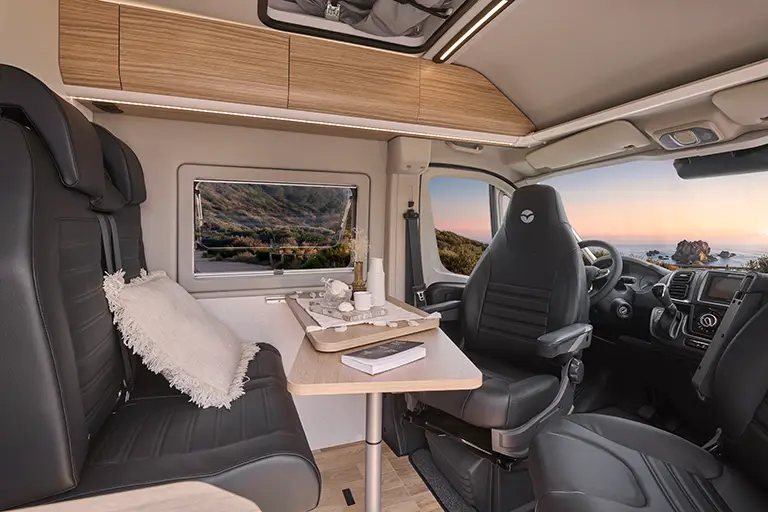 Intérieur d'un fourgon aménagé V600G avec banquette en tissu noir, table en bois et sièges cabine pivotants.