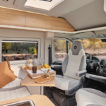 Intérieur d'un fourgon aménagé V630S avec banquette en tissu clair, table en bois et sièges cabine pivotants - décoration Pyla